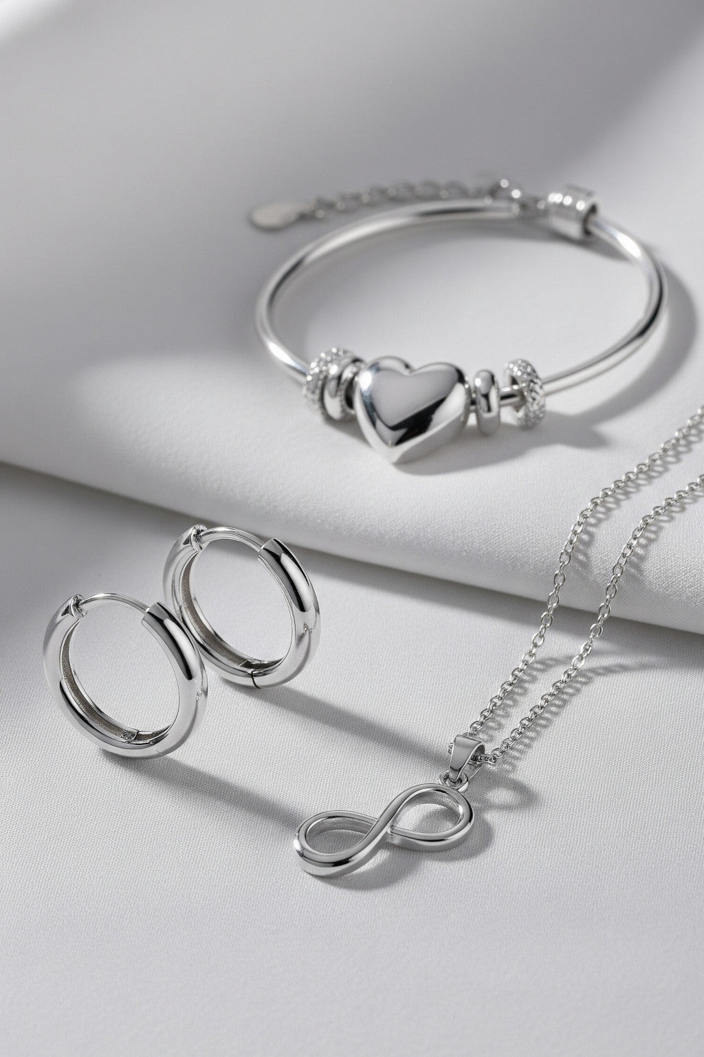 Silver bracelet, hoop earrings, and infinity necklace on a light gray background
