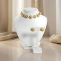 Gold plated silver choker necklace in flower shaped motifs and matching earrings on a white jewelry stand with a soft beige background