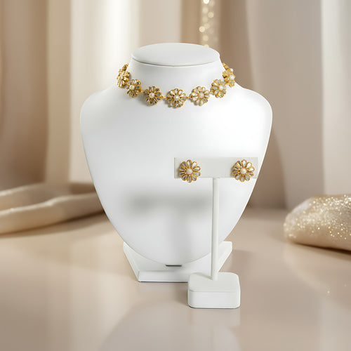 Gold plated silver choker necklace in flower shaped motifs and matching earrings on a white jewelry stand with a soft beige background