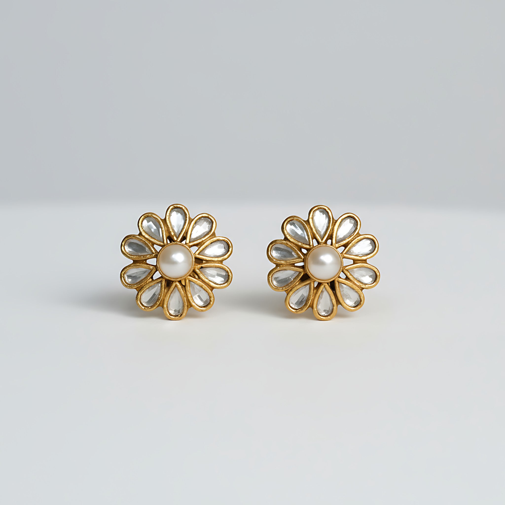 Gold plated silver flower-shaped earrings with pearl centers on a light gray background