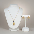 Jewelry set with pearl and gold plated silver necklace with blue gemstone and matching earrings on white stands against a neutral background