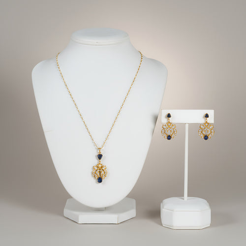 Jewelry set with pearl and gold plated silver necklace with blue gemstone and matching earrings on white stands against a neutral background