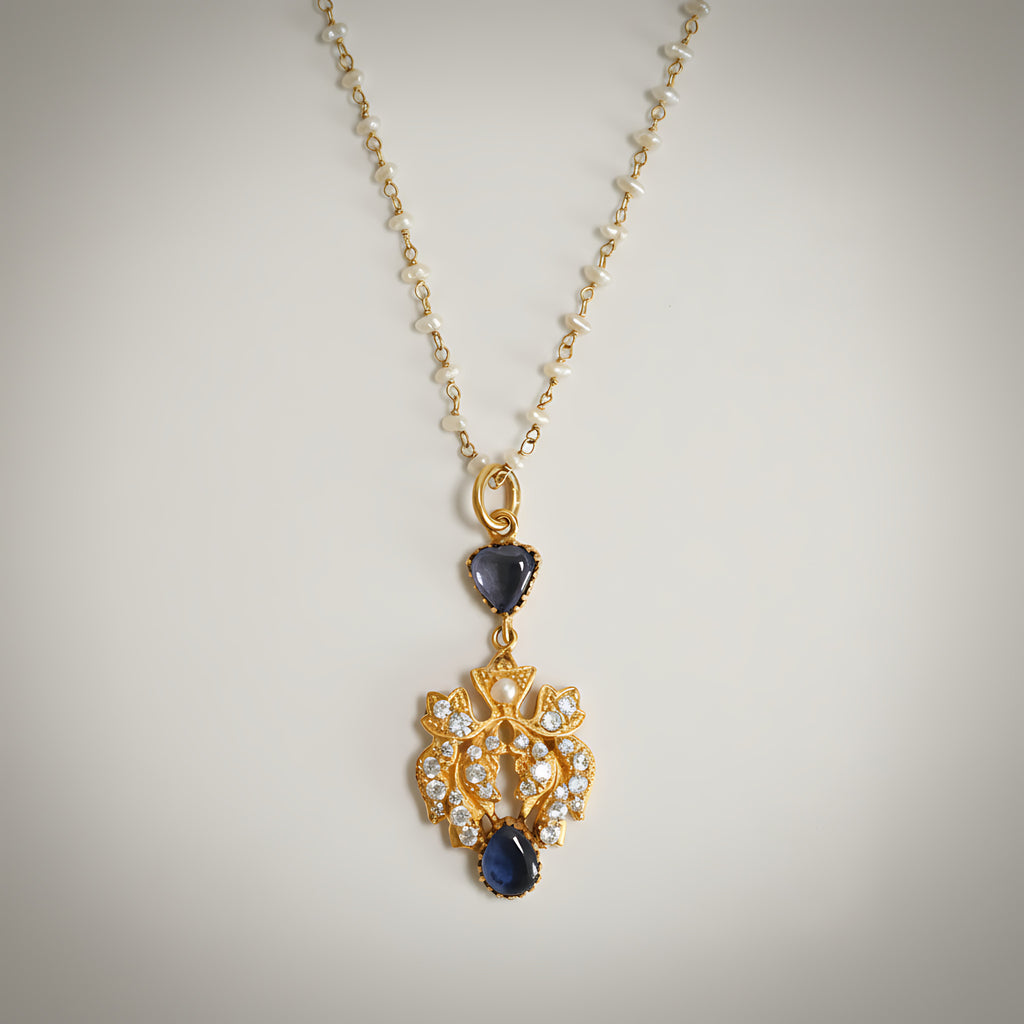 Pearl and gold plated silver necklace with a pendant with blue stones on a light gray background