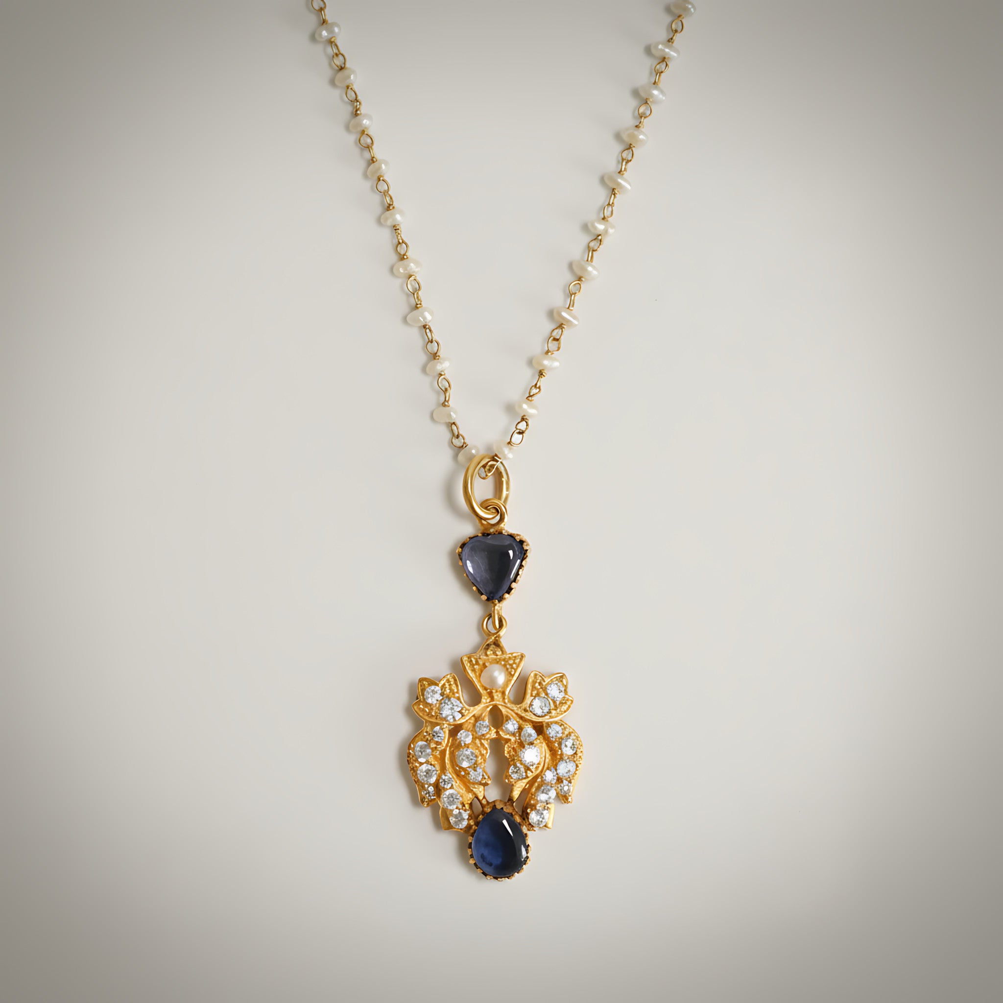 Pearl and gold plated silver necklace with a pendant with blue stones on a light gray background