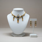 Gold necklace with blue and green gemstones on a white mannequin bust and matching earrings on a stand.