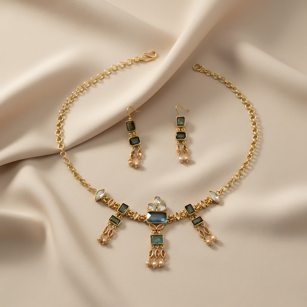 Gold necklace with blue and green gemstones on a white mannequin bust and matching earrings on a beige fabric background