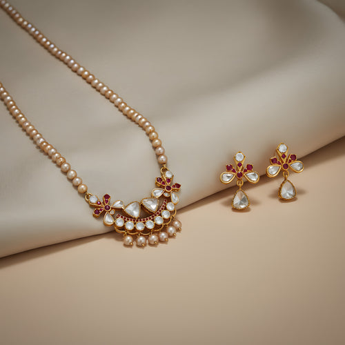 Pearl necklace  with a decorative gold plated silver and gemstone pendant and matching earrings on a beige fabric background