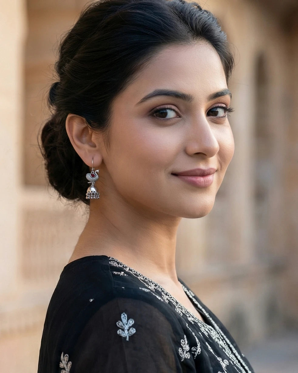 A woman in a black outfit wearing silver peacock jhumka earrings.