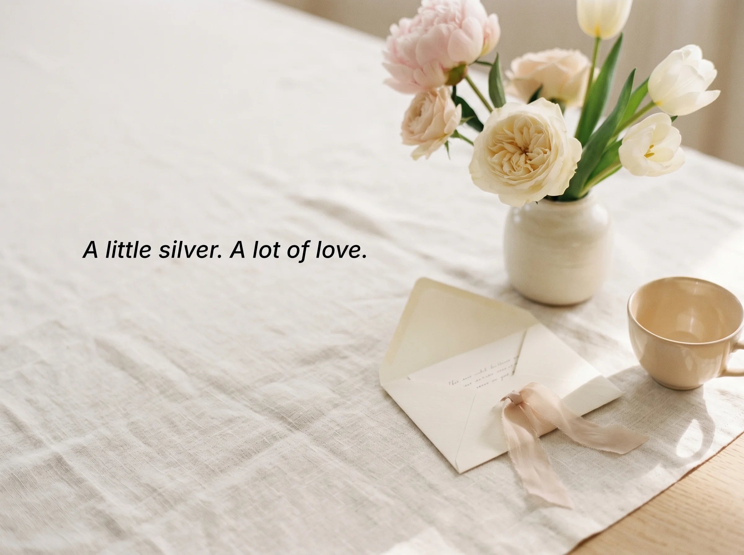 Vase of flowers on a table with a cup and card, text 'A little silver. A lot of love.'