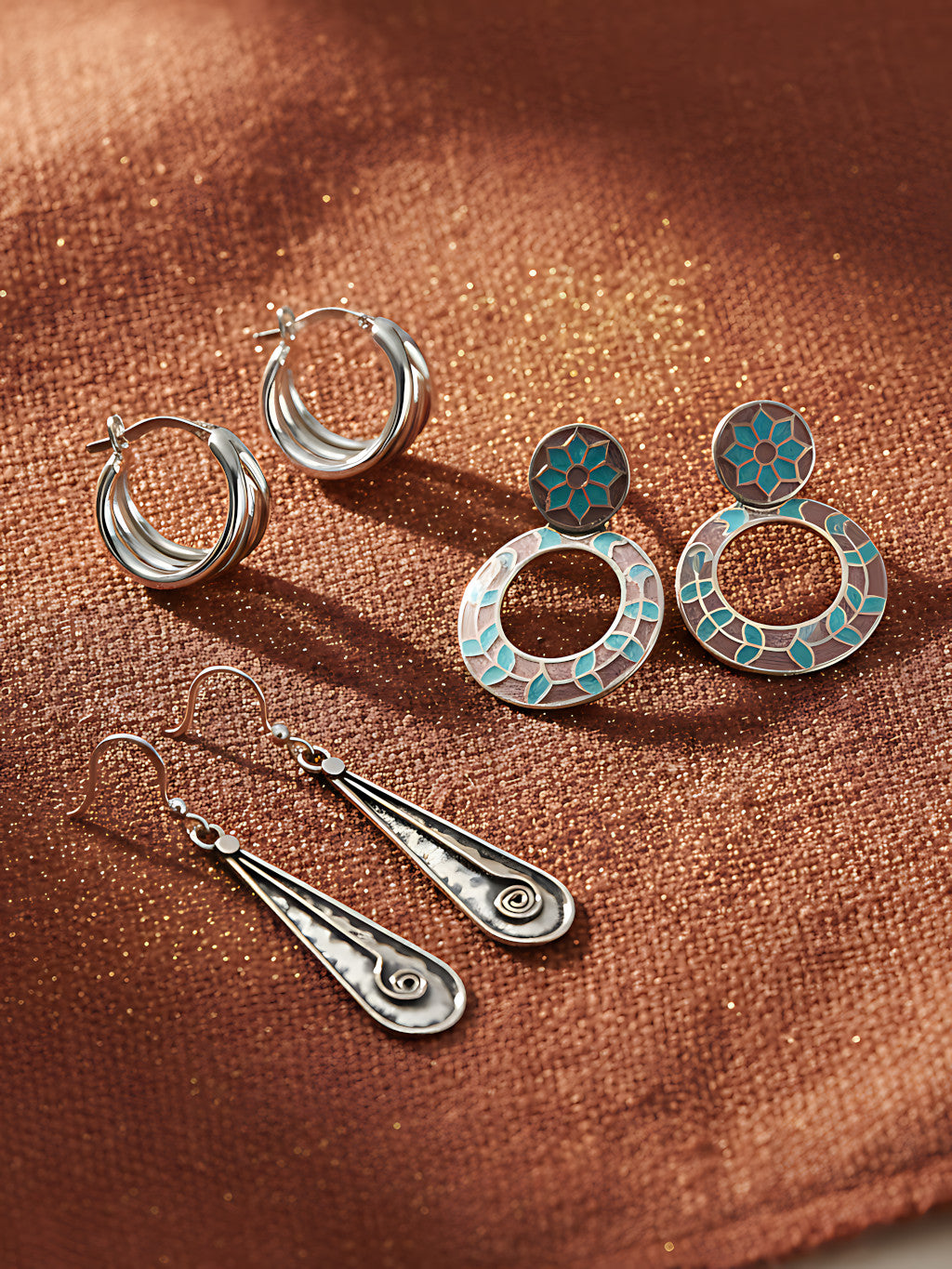 Three pairs of silver earrings on a brown fabric background
