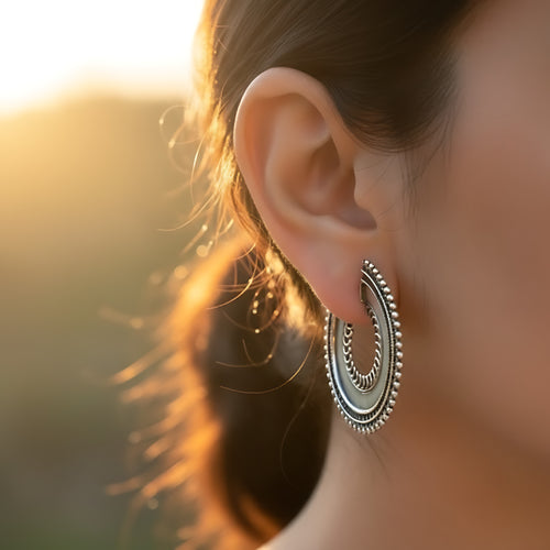 Close-up of an ear wearing an oxidized silver beaded crescent half hoop stud earring with a blurred background