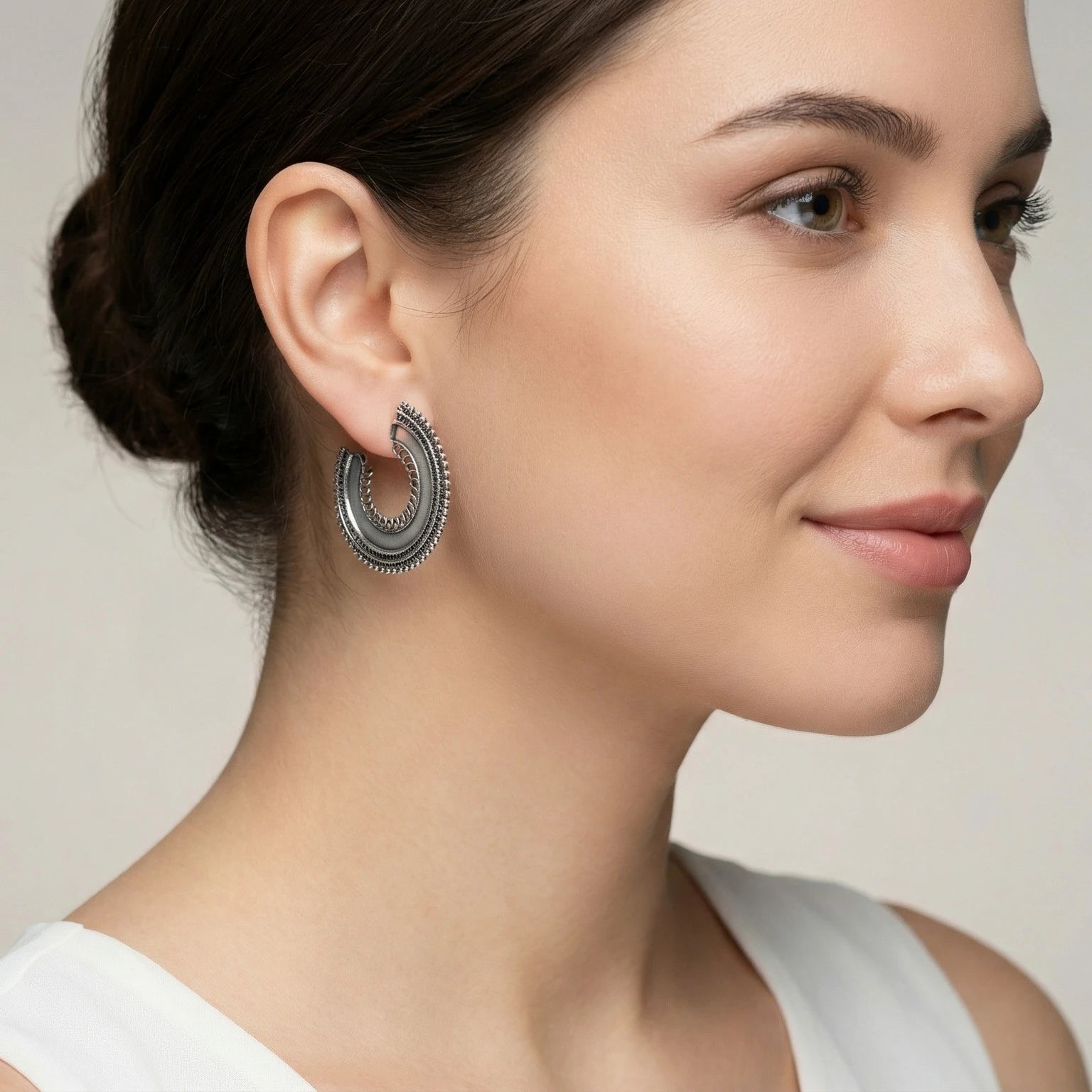 Close-up of an ear wearing an oxidized silver beaded crescent half hoop stud earring with a plain background