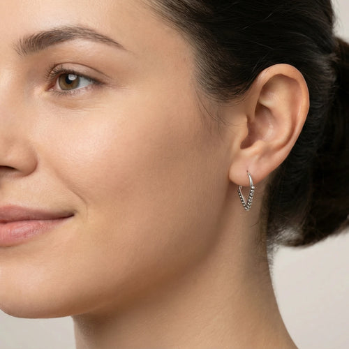 Close-up of a woman wearing a v-shaped with beaded accent silver hoop earring against a neutral background