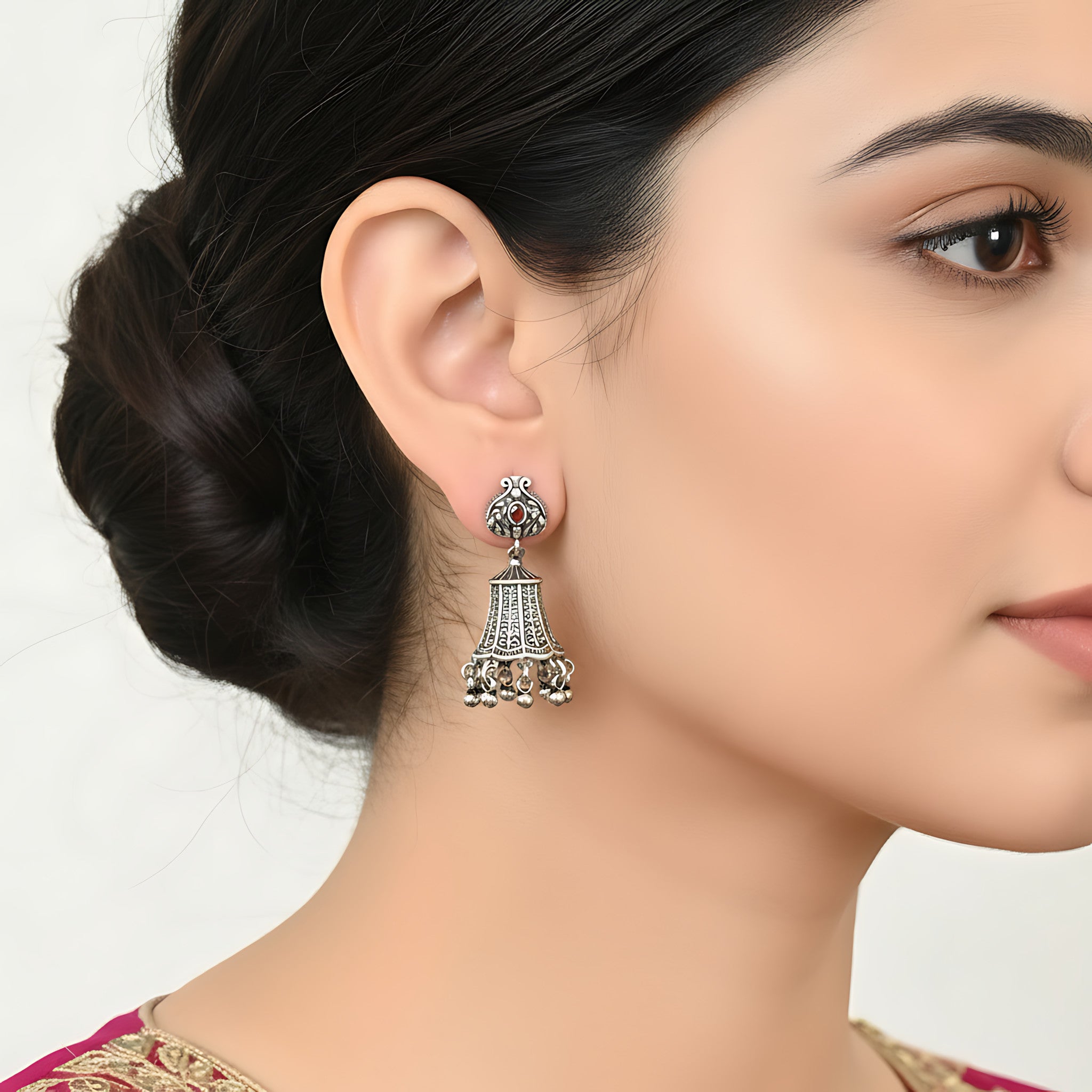 Close-up of a woman wearing a bell-shaped oxidized silver jhumka earring with a white background