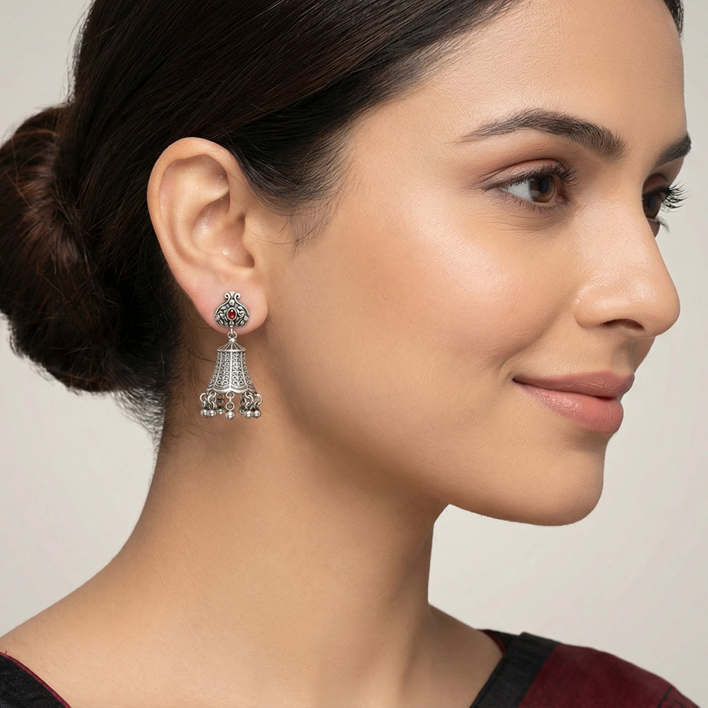 Close-up of a woman wearing a bell-shaped oxidized silver jhumka earring with a grey background