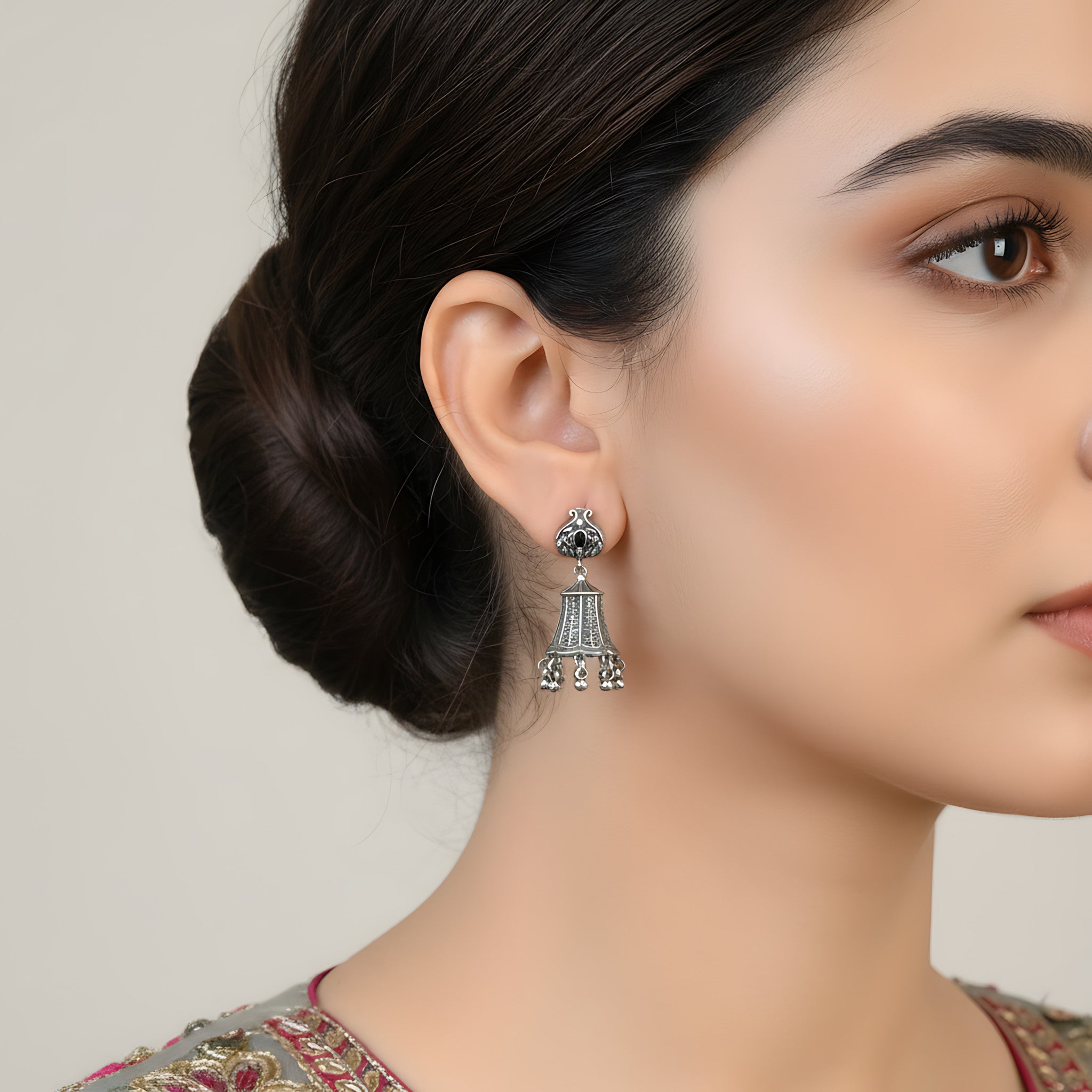 Close-up of a woman wearing an oxidized silver bell-shaped jhumka earring with a neutral background