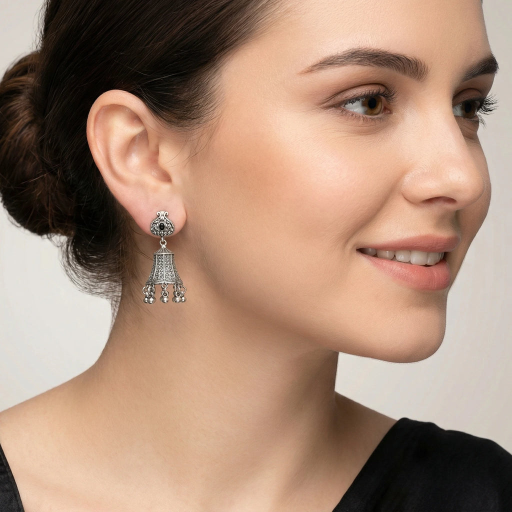 Close-up of a woman wearing a bell-shaped oxidized silver jhumka earring with a grey background