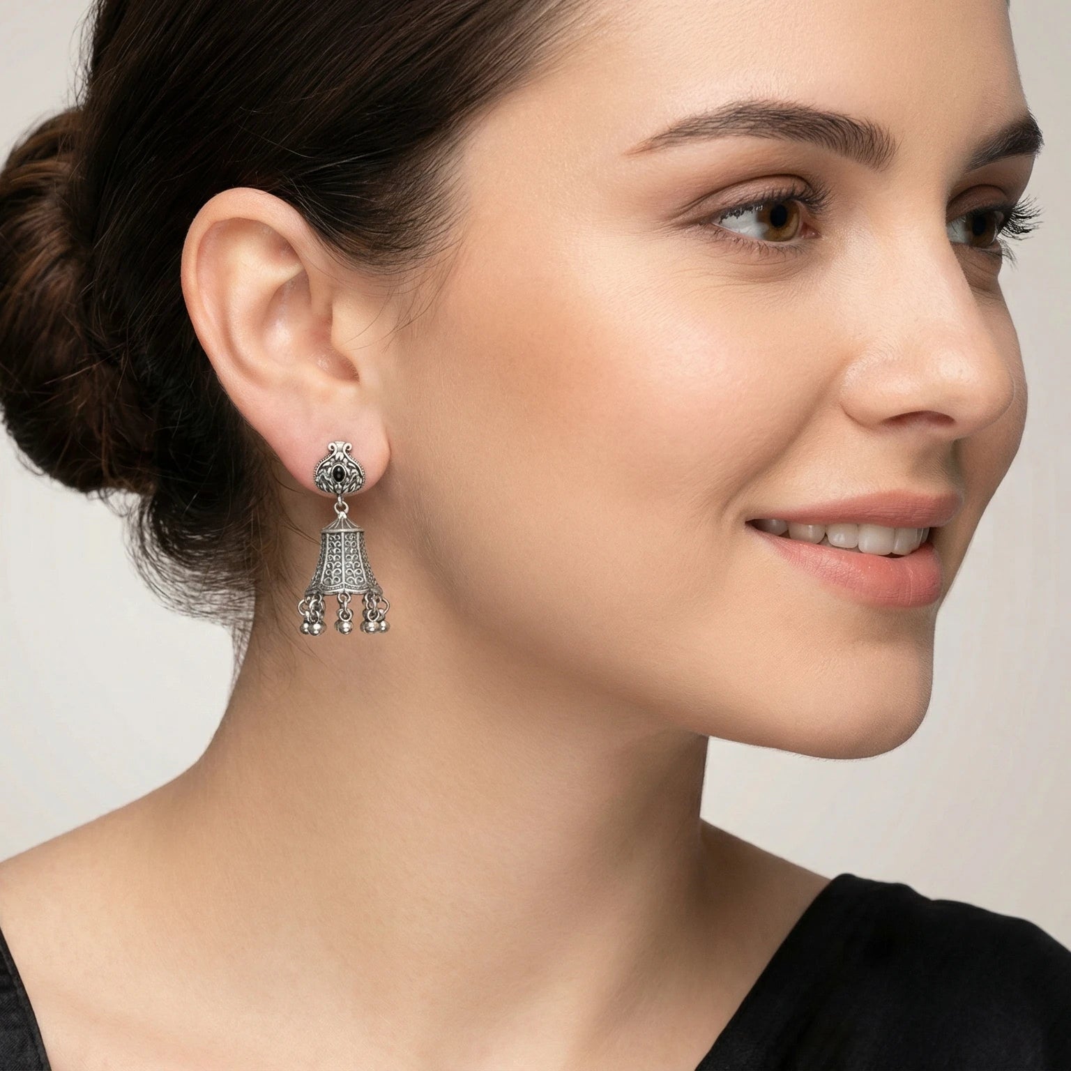 Close-up of a woman wearing a bell-shaped oxidized silver jhumka earring with a grey background