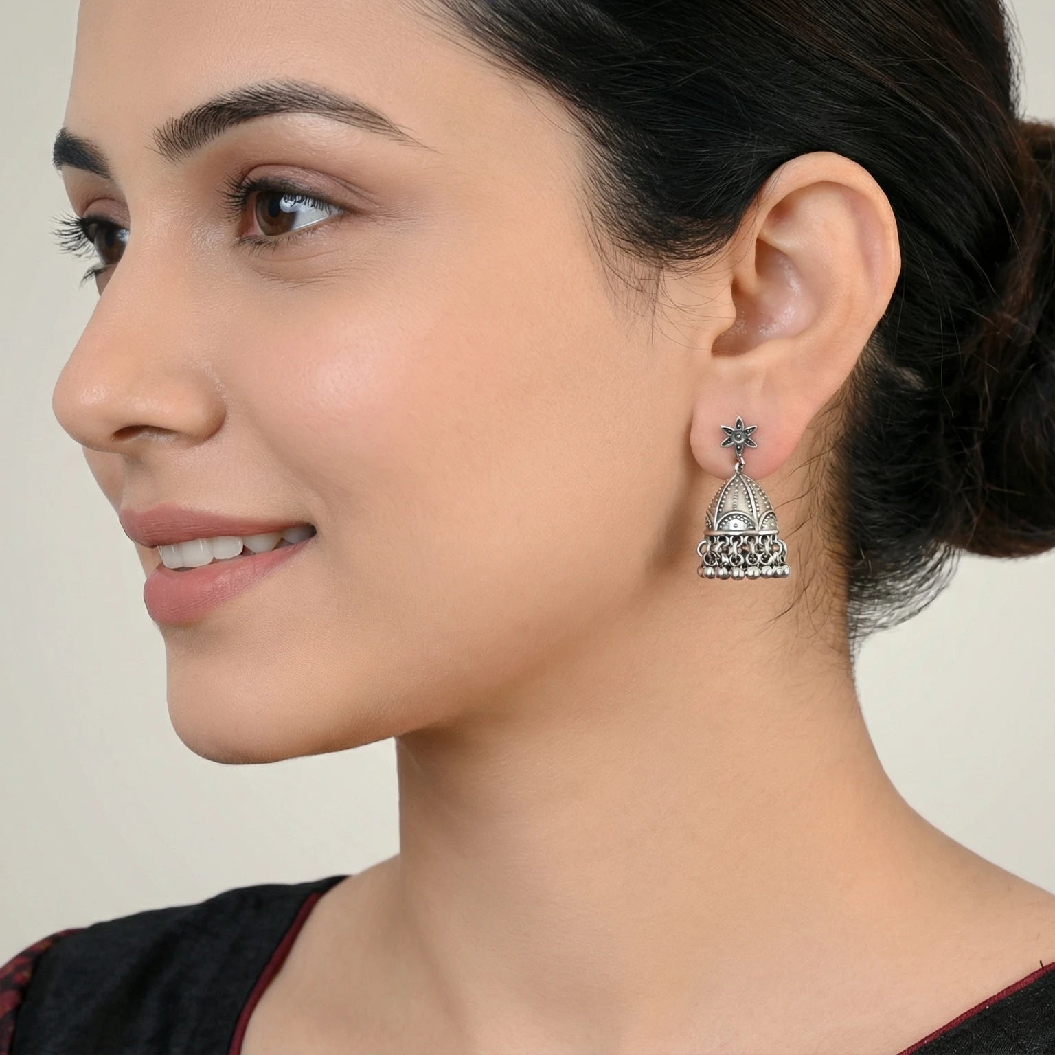 Close-up of a woman wearing an oxidized silver jhumka earring with a neutral background