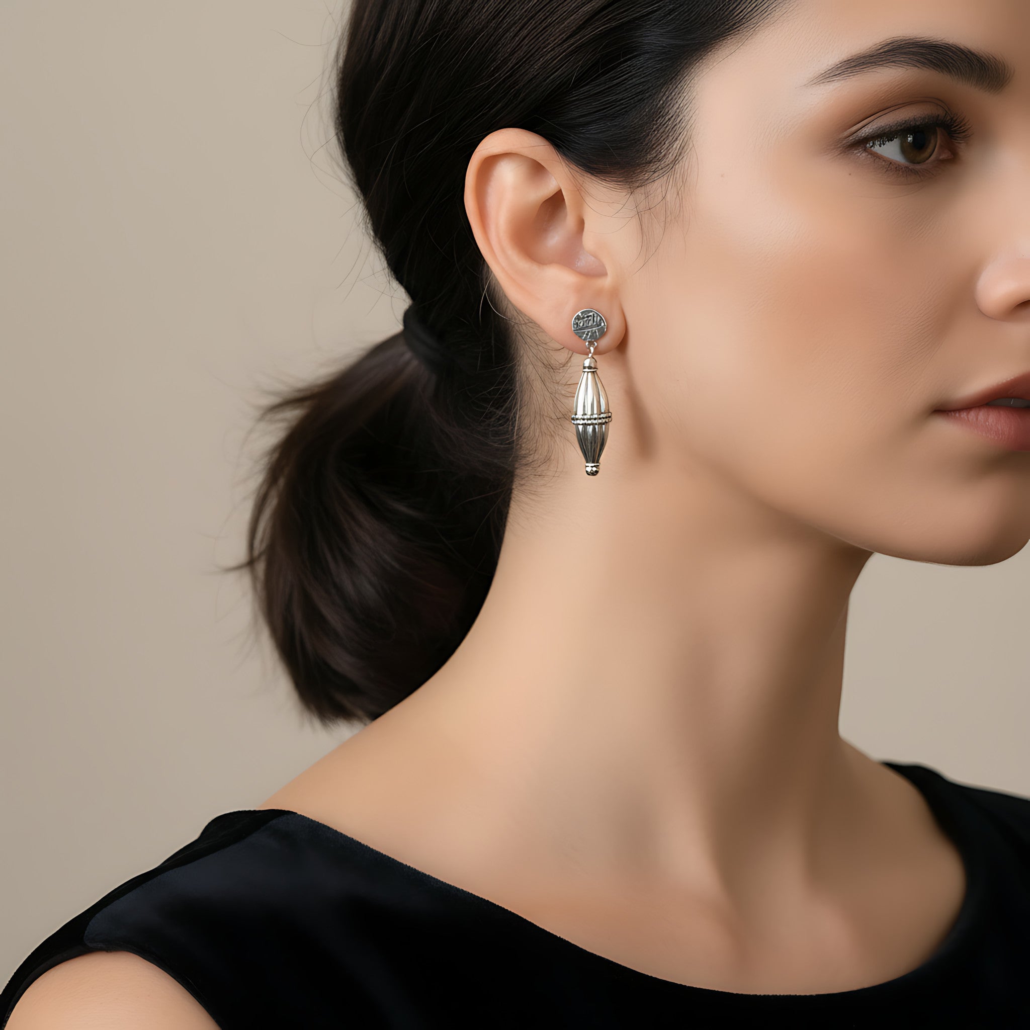 Close-up of a woman wearing a dholki-shaped oxidized silver stud earring with a neutral background