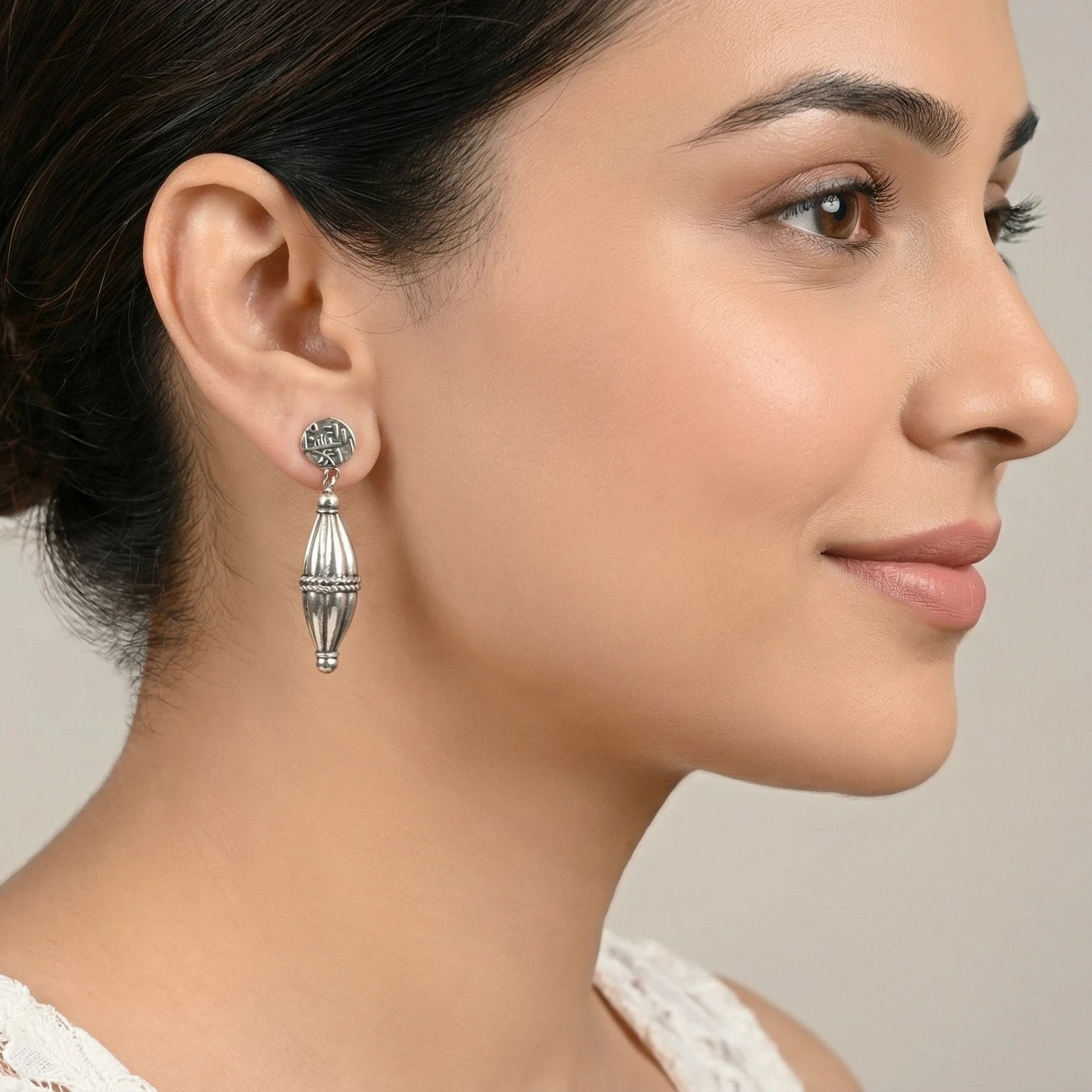 Close-up of a woman wearing a dholki-shaped oxidized silver stud earring with a neutral background