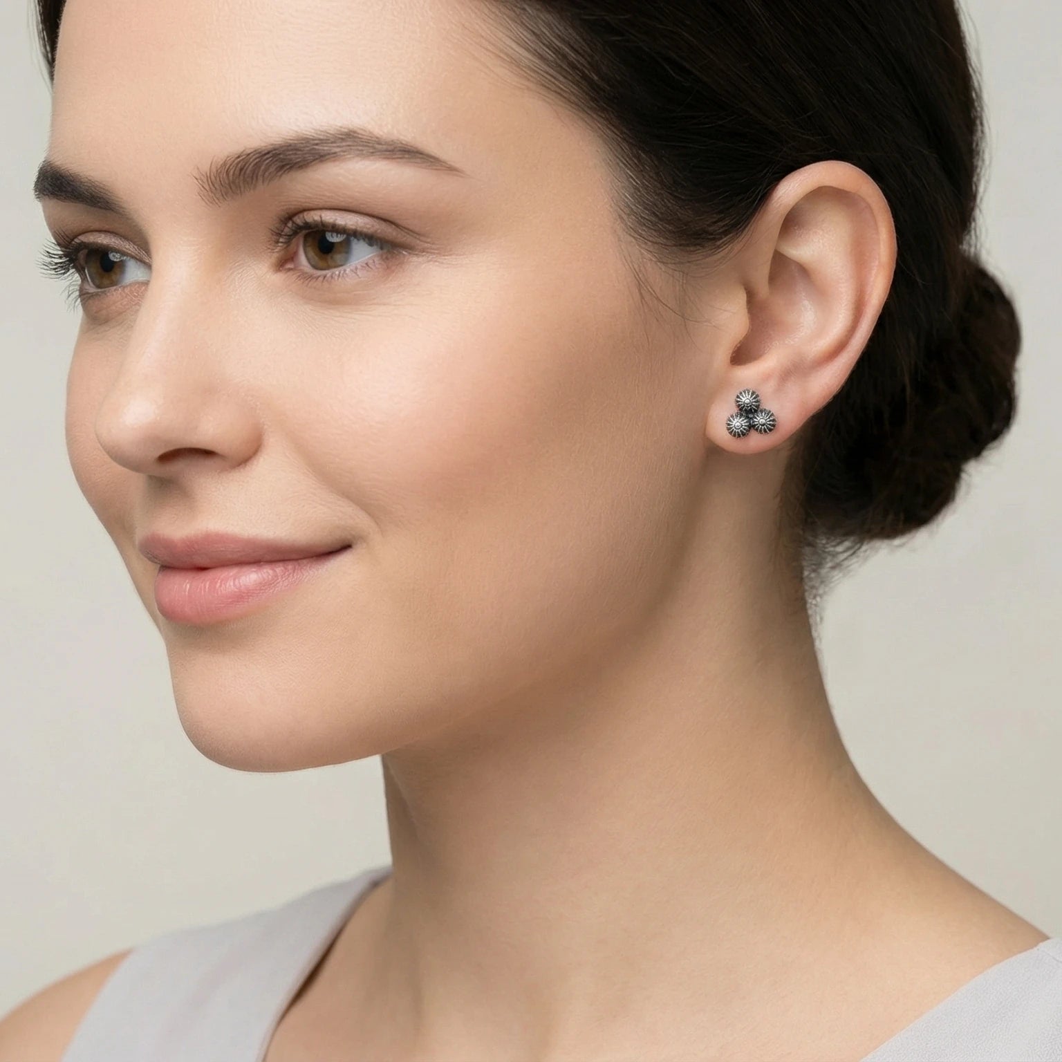 Close-up of a woman wearing a pair of 3 dome shaped oxidized silver earring with a neutral background