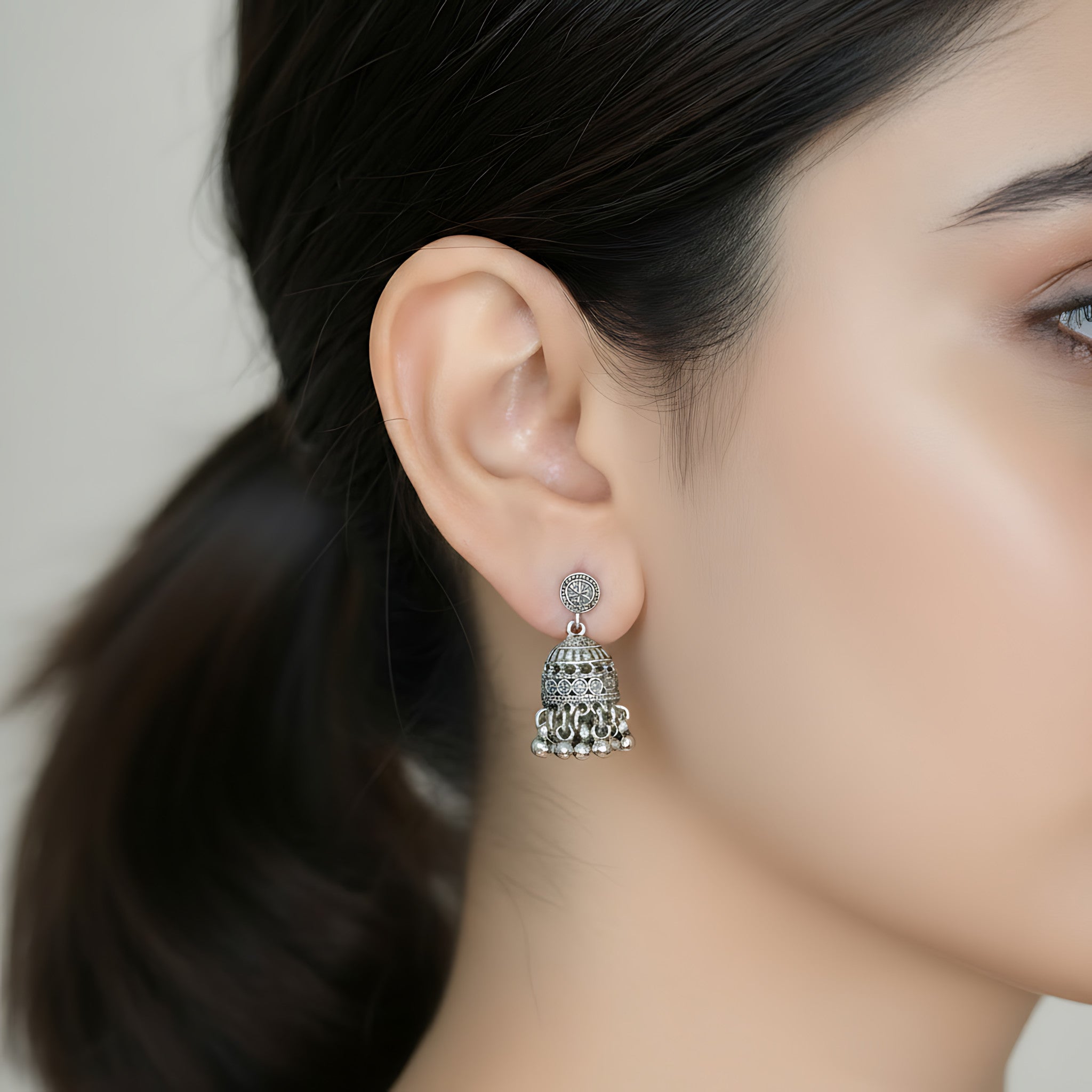 Close-up of a woman wearing a small oxidized silver jhumka earring with intricate design.
