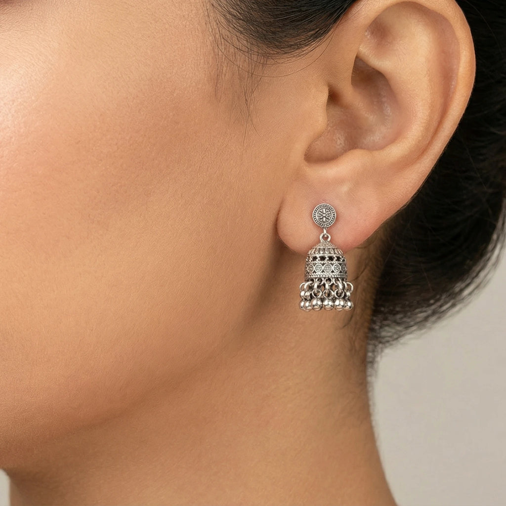 Close-up of a woman wearing a small oxidized silver jhumka earring with intricate design.