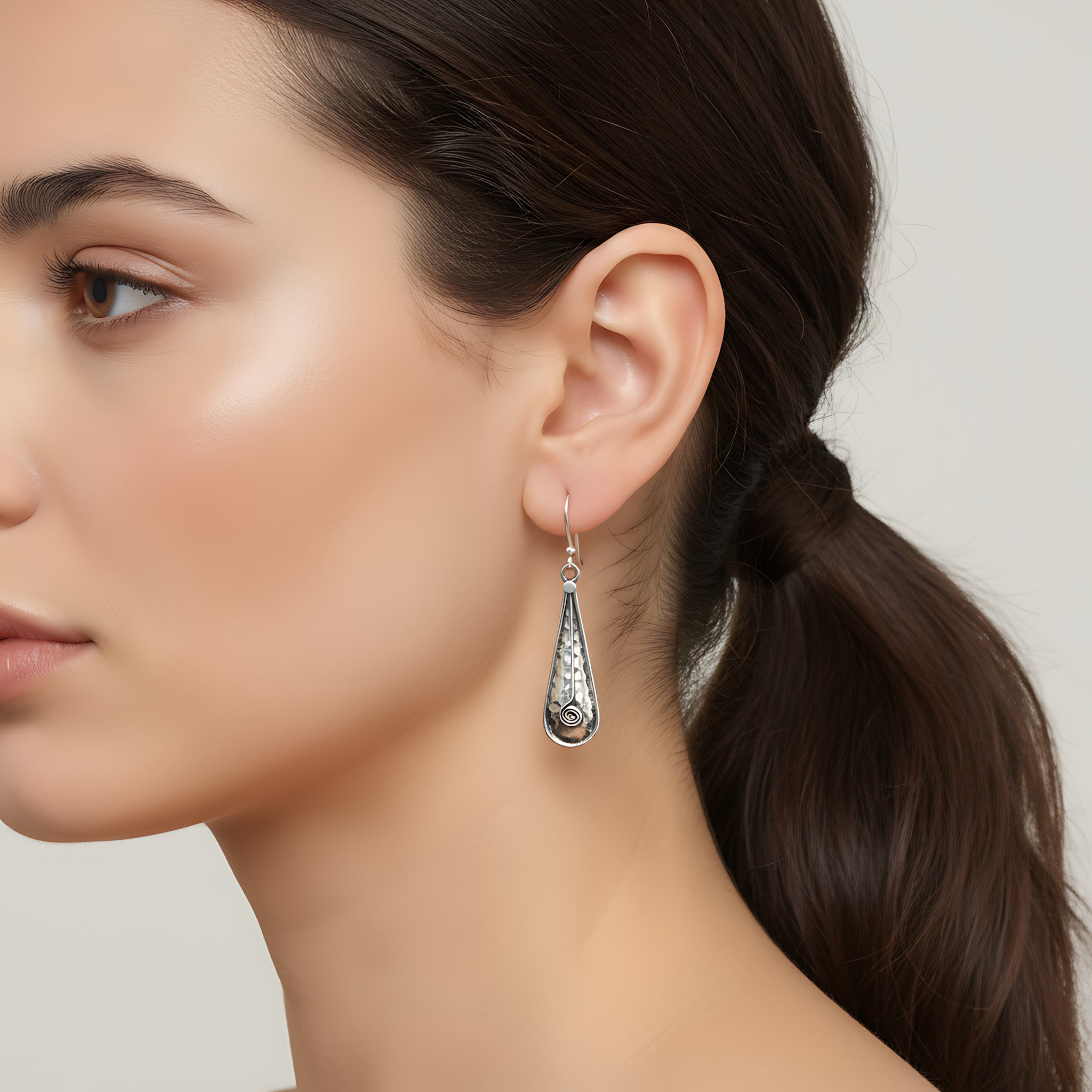 Close-up of a woman wearing an oxidized silver hammered teardrop earring with a blurred background