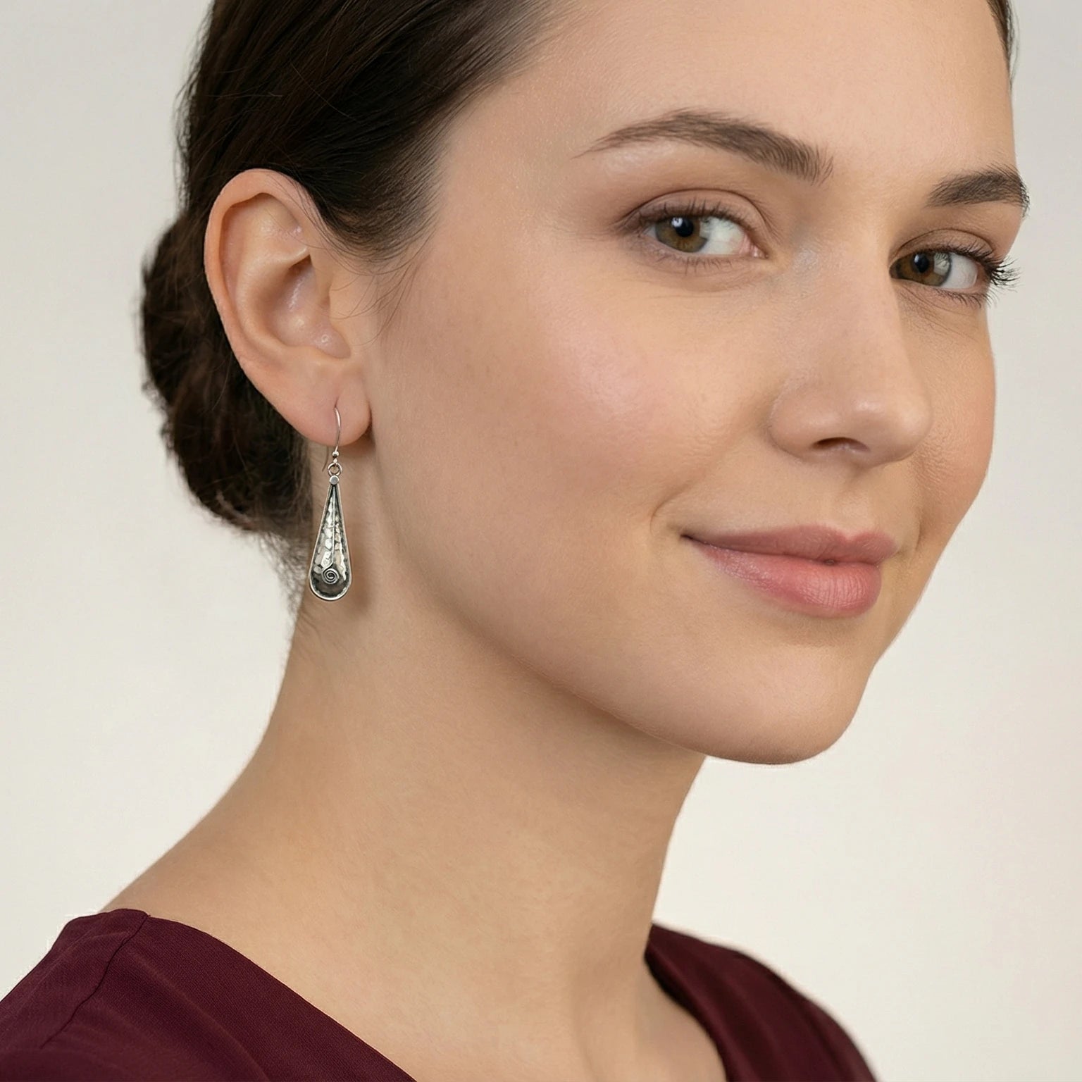 Close-up of a woman wearing a Oxidized Silver Hammered Teardrops Dangle Earrings against a neutral background