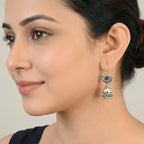 Close-up of a woman wearing an oxidized silver peacock jhumka earring with a blue gemstone on a neutral background