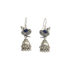 Pair of silver peacock jhumka earrings with blue stones on a white background