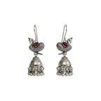 Pair of oxidized silver peacock  jhumka earrings with red gemstones on a white background