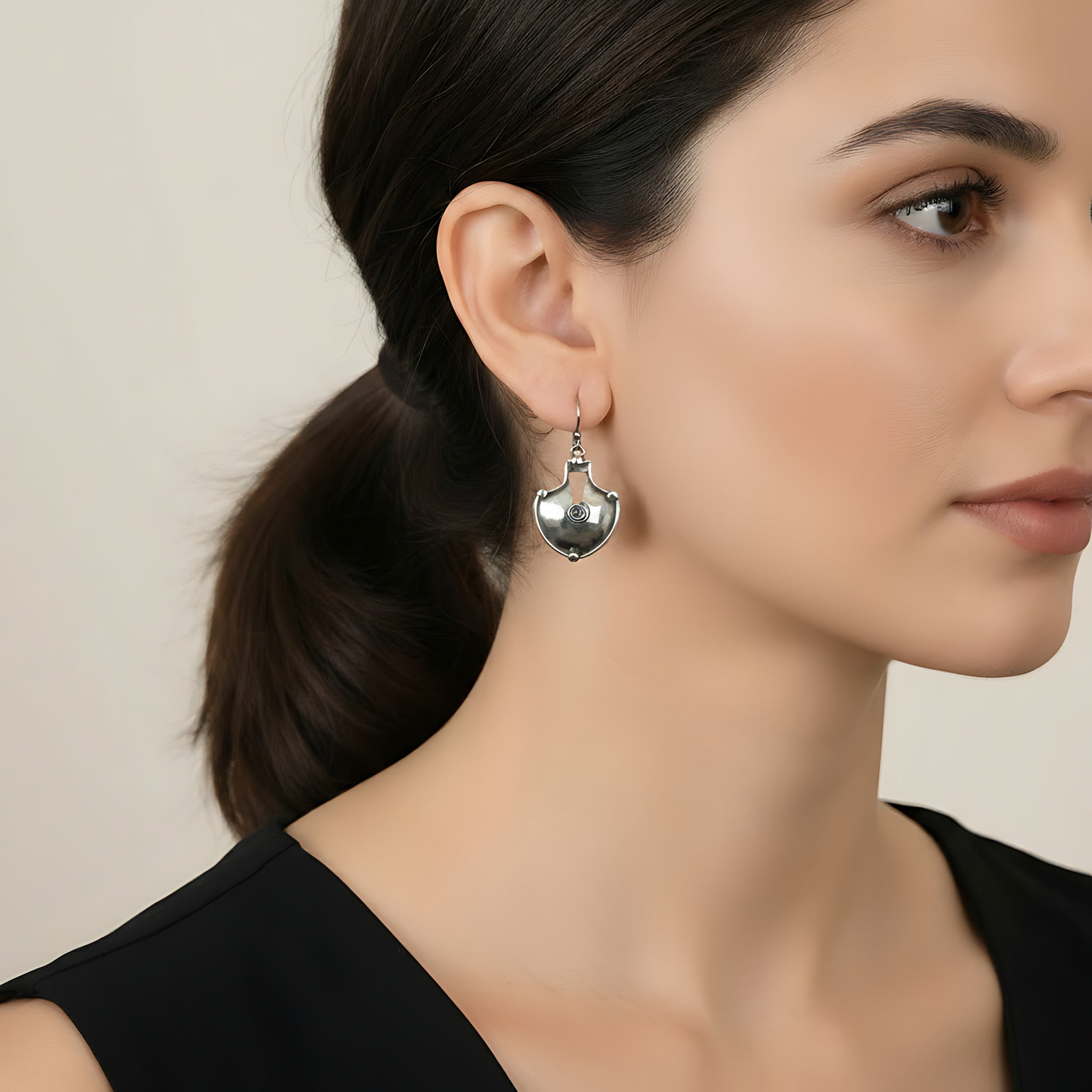 Woman wearing a shield shaped oxidized silver earring with a neutral background