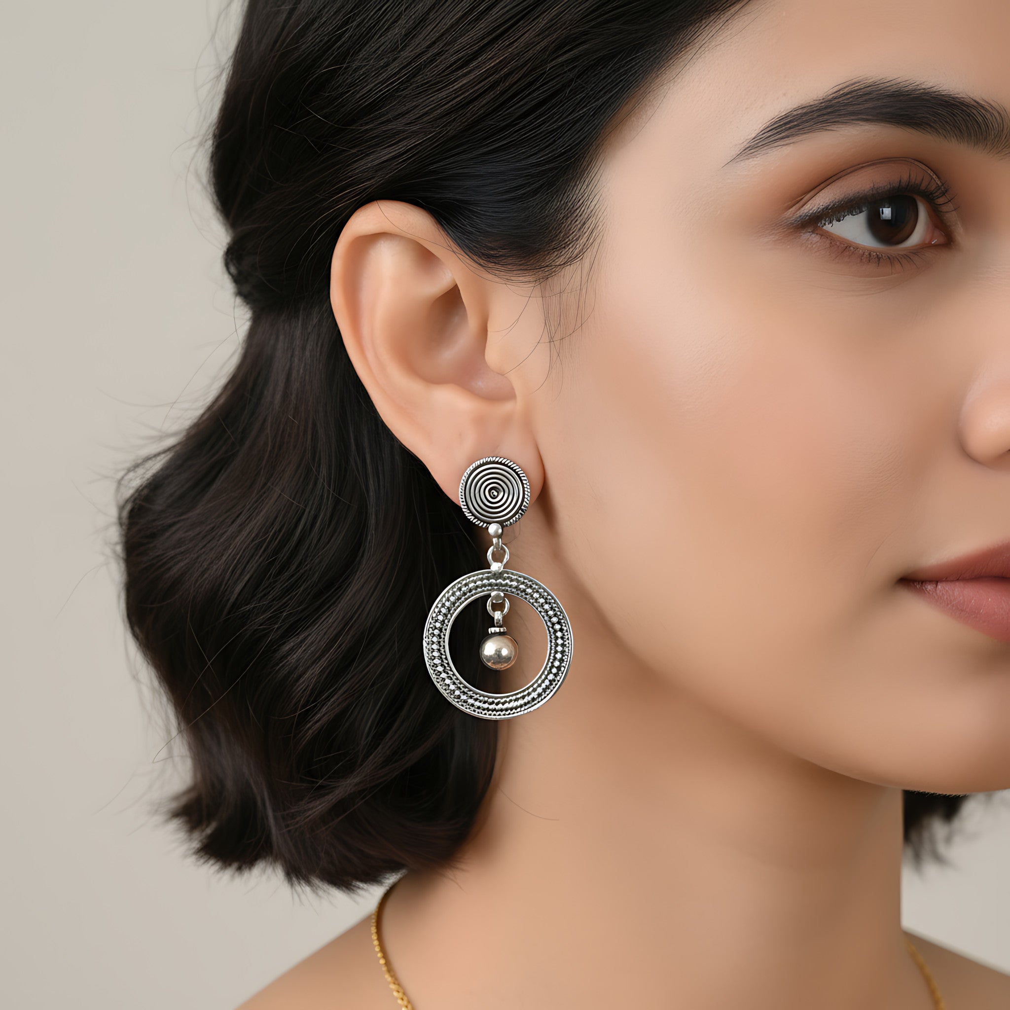 Close-up of a woman wearing an oxidized silver spiral orbit stud earring against a plain background