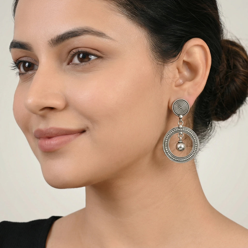 Close-up of a woman wearing an oxidized silver spiral orbit stud earring against a plain background