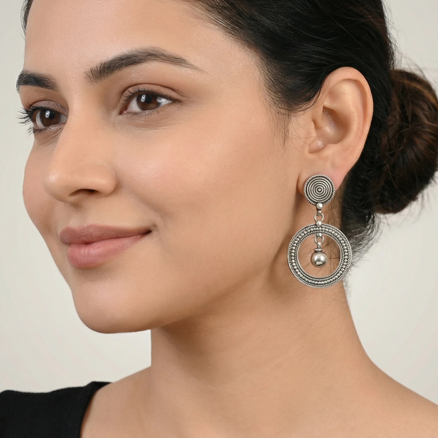 Close-up of a woman wearing an oxidized silver spiral orbit stud earring against a plain background