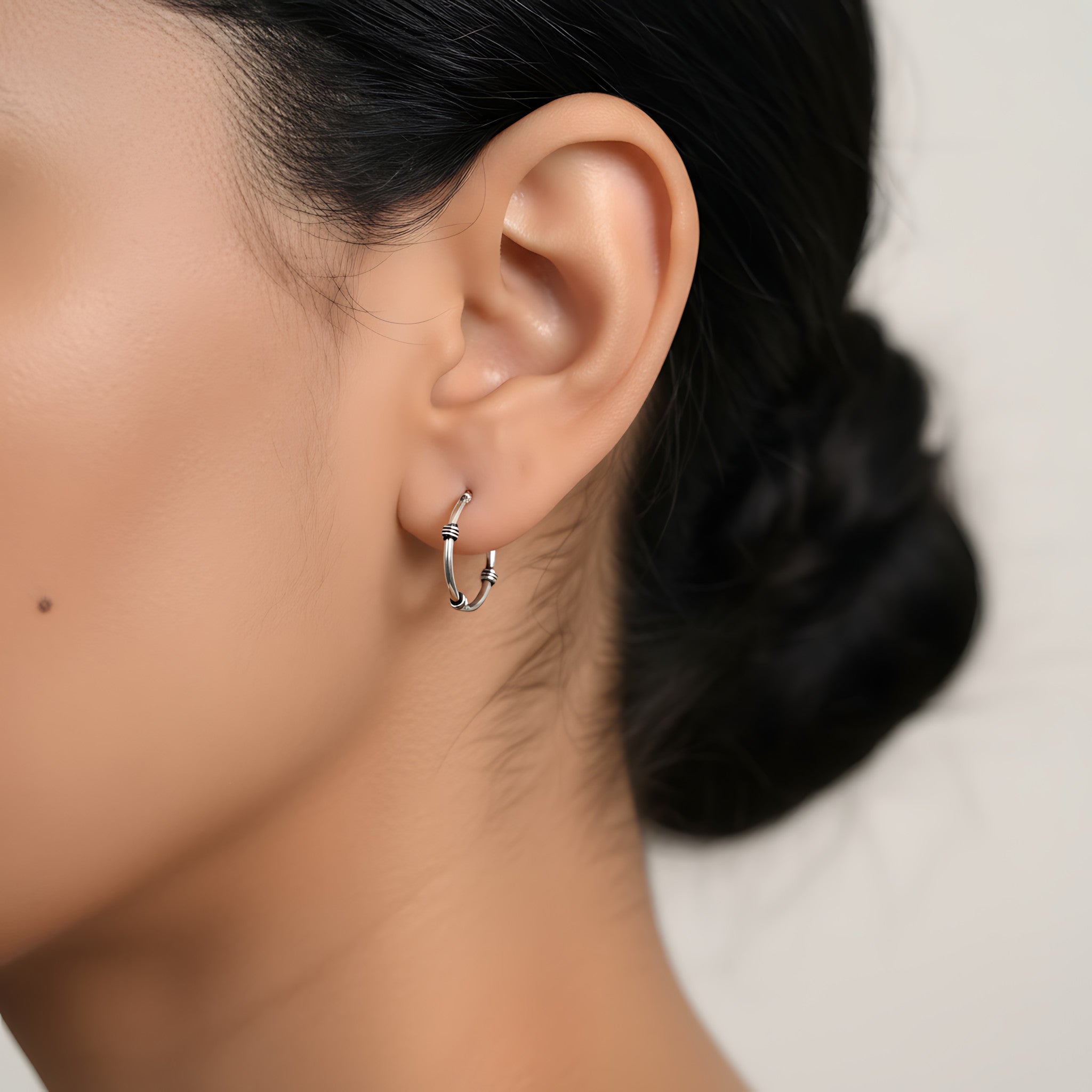 Close-up of an ear wearing a triple band Bali oxidized silver hoop earring with a blurred background