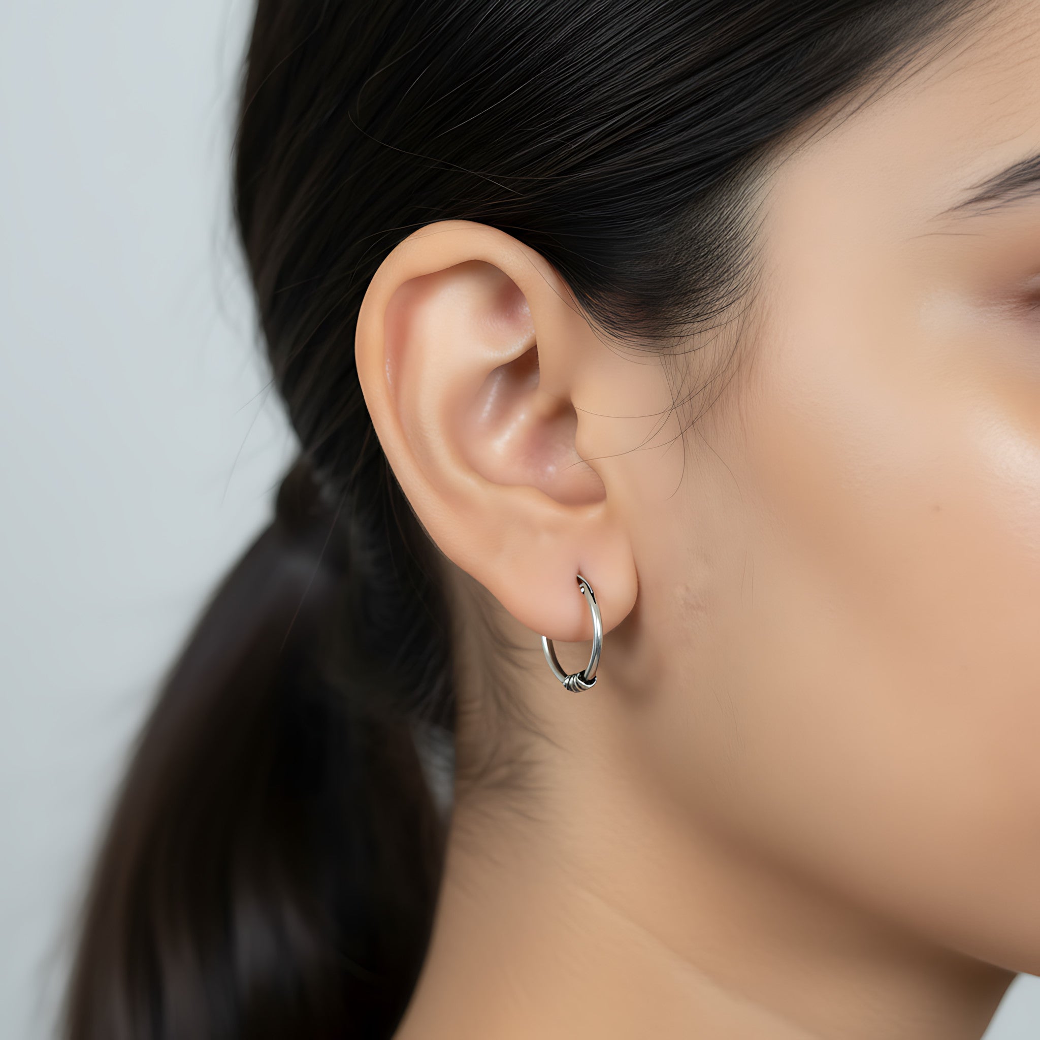 Close-up of a person wearing a triple bead Bali oxidized silver hoop earring with a neutral background