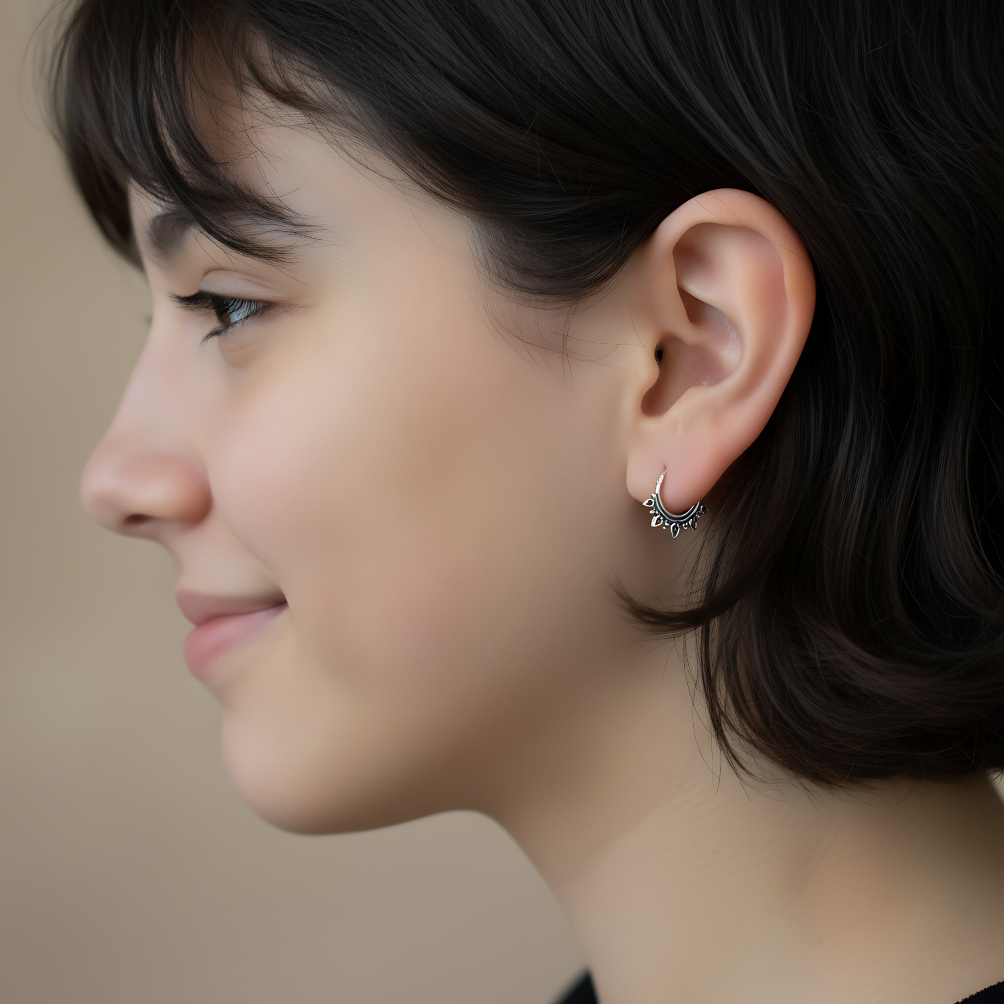 Closeup of a girl wearing a silver Bali hoop earring on a neutral background