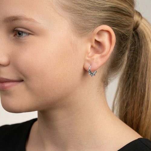 Closeup of a girl wearing a silver Bali hoop earring on a neutral background