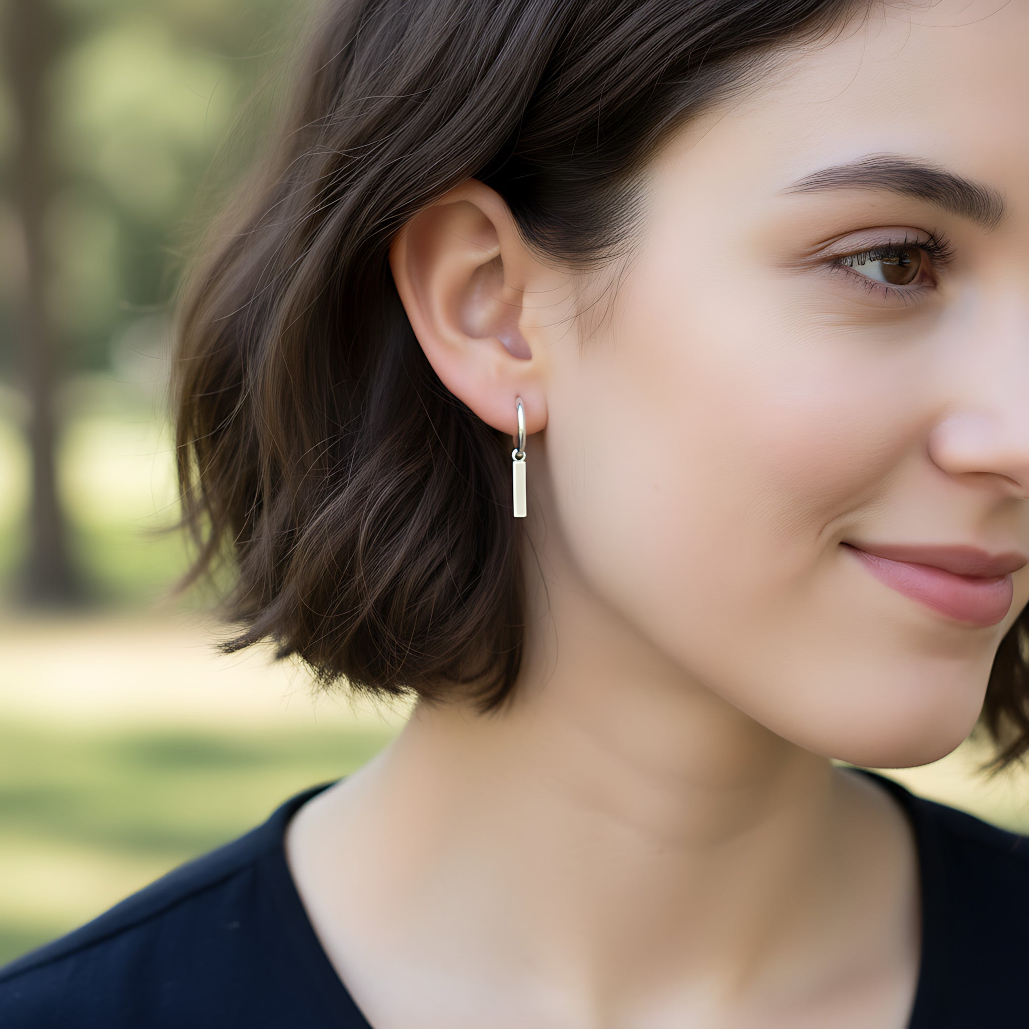 Close-up of a woman wearing a silver bar charm hoop earring outdoors