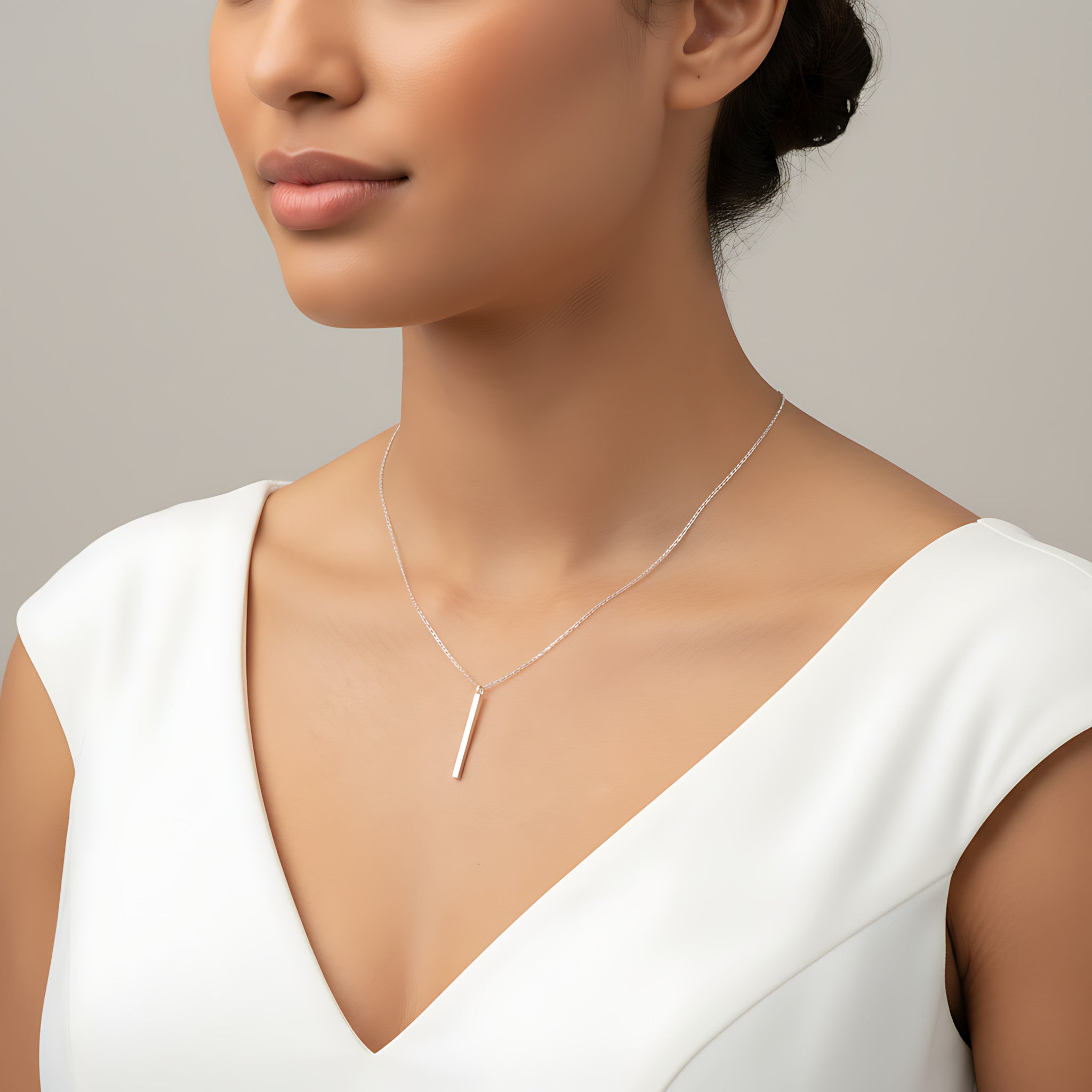 Closeup of a female wearing a silver necklace with a bar pendant against a neutral background