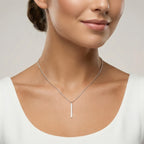Closeup of a female wearing a silver necklace with a bar pendant against a neutral background