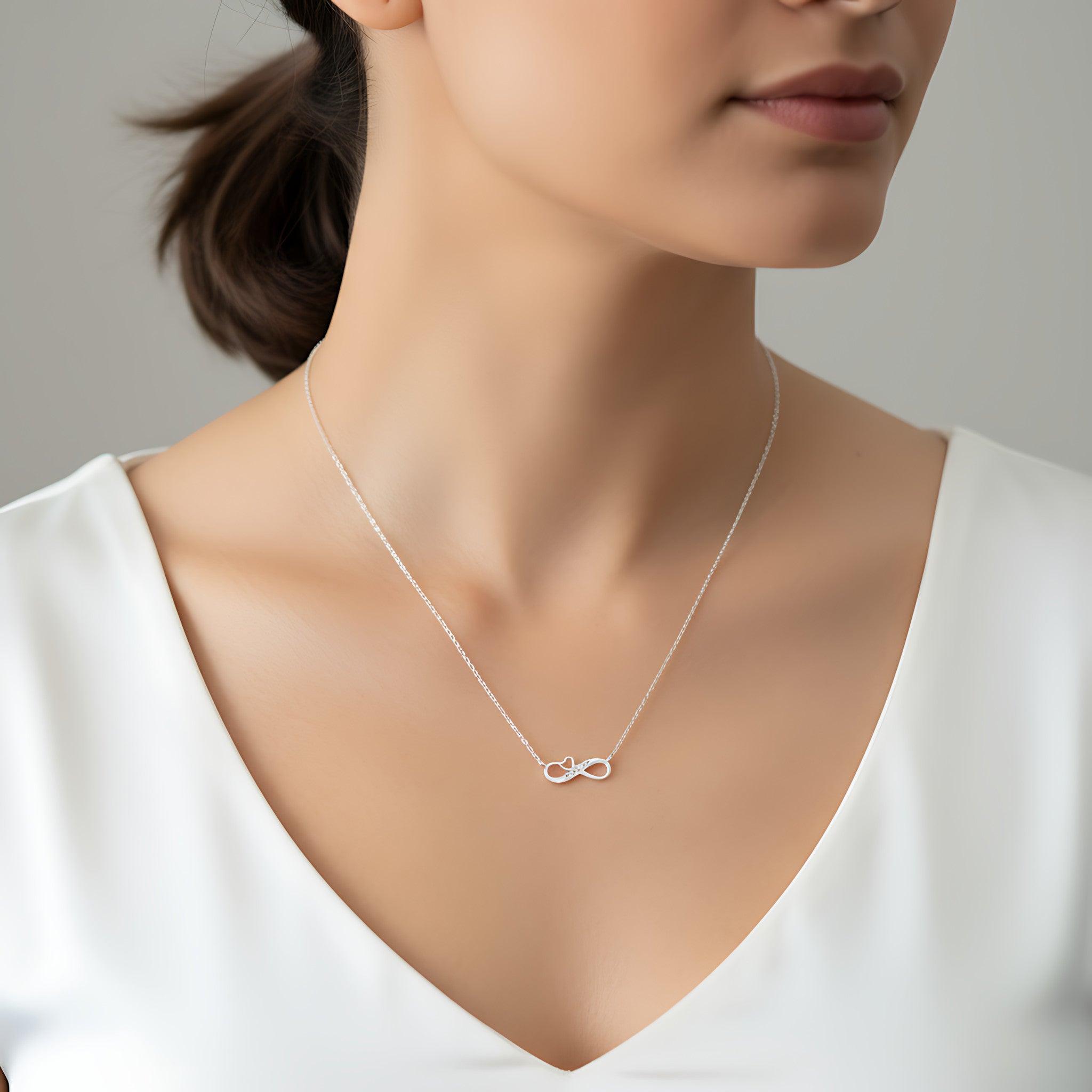 Woman wearing a silver infinity necklace with a heart and an engraving "Best Mom" against a neutral background