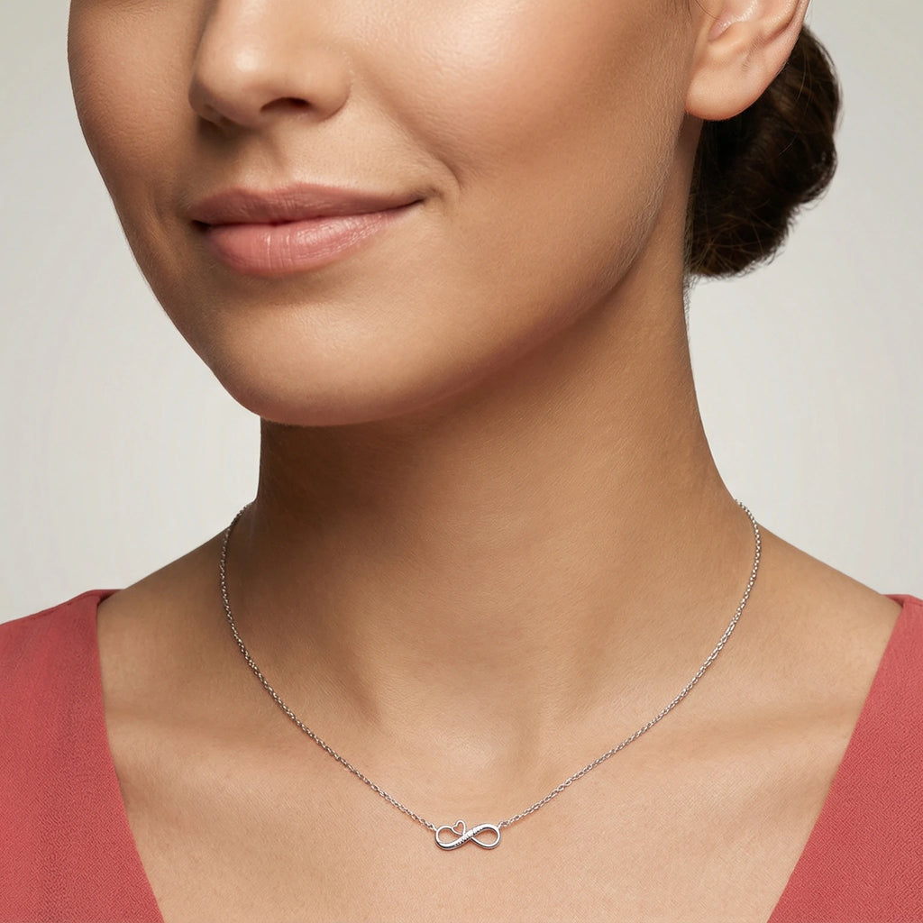 Woman wearing a silver infinity necklace with a heart and an engraving "Best Mom" against a neutral background