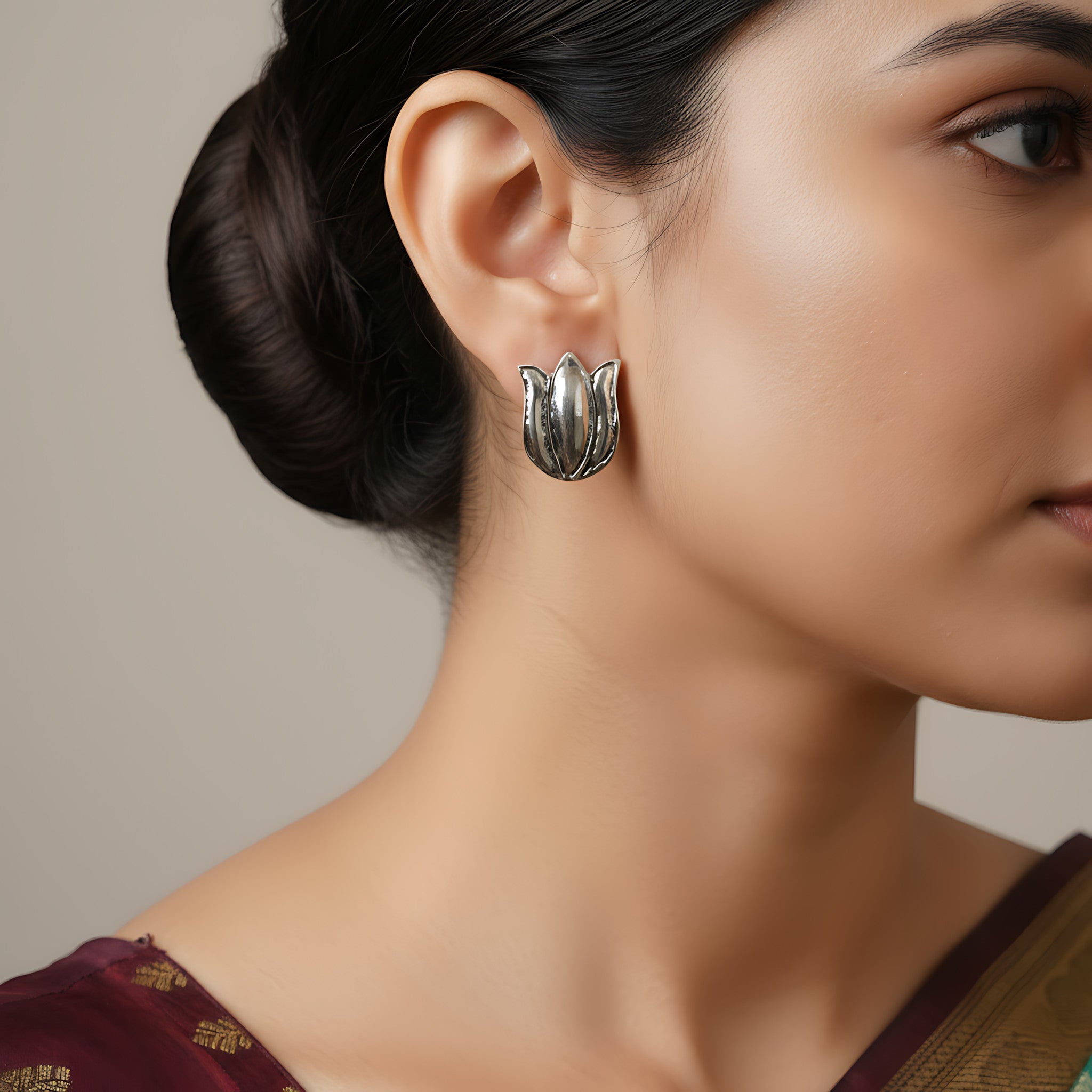 Close-up of a woman wearing silver lotus-shaped stud earring against a neutral background