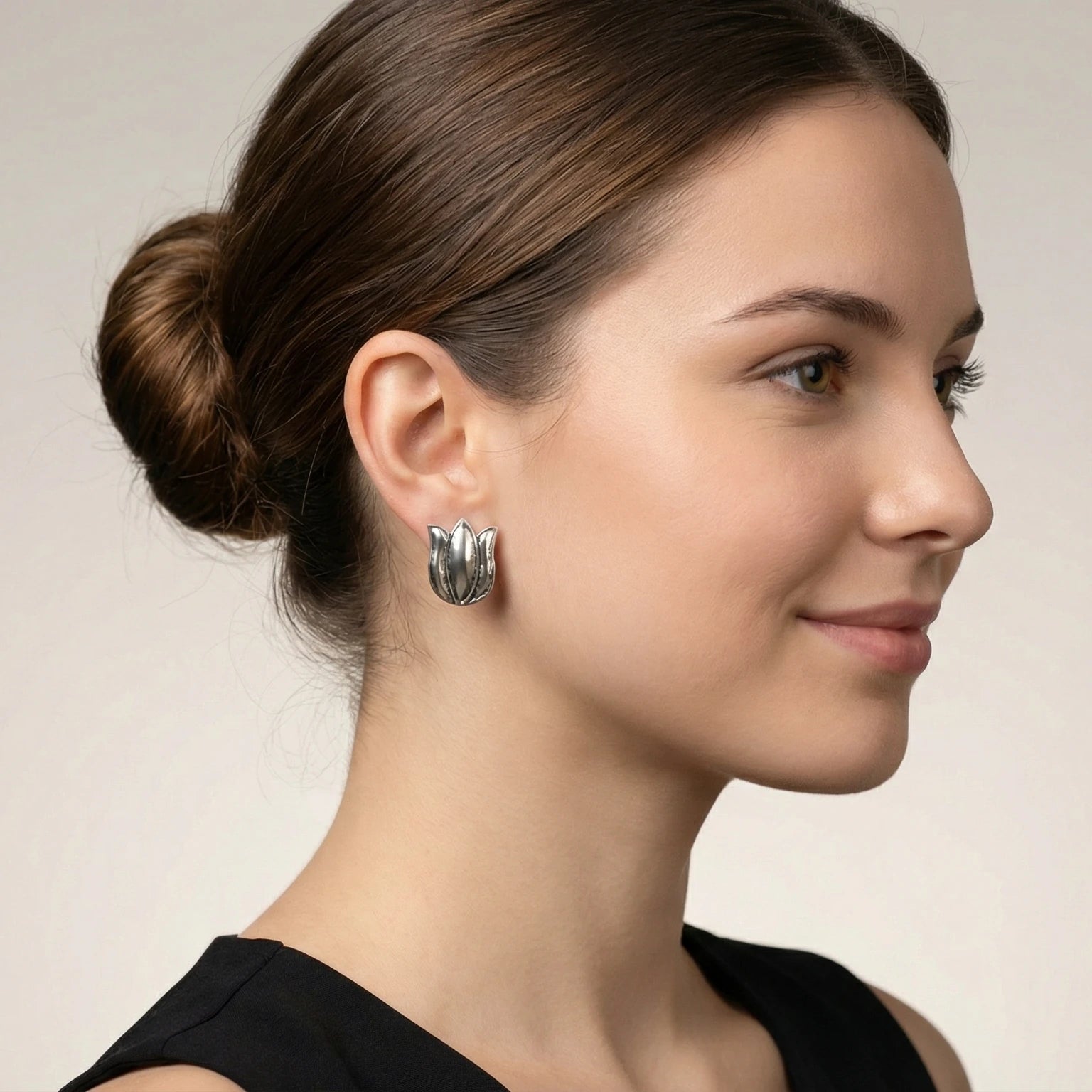 Close-up of a woman wearing silver lotus-shaped stud earring against a neutral background