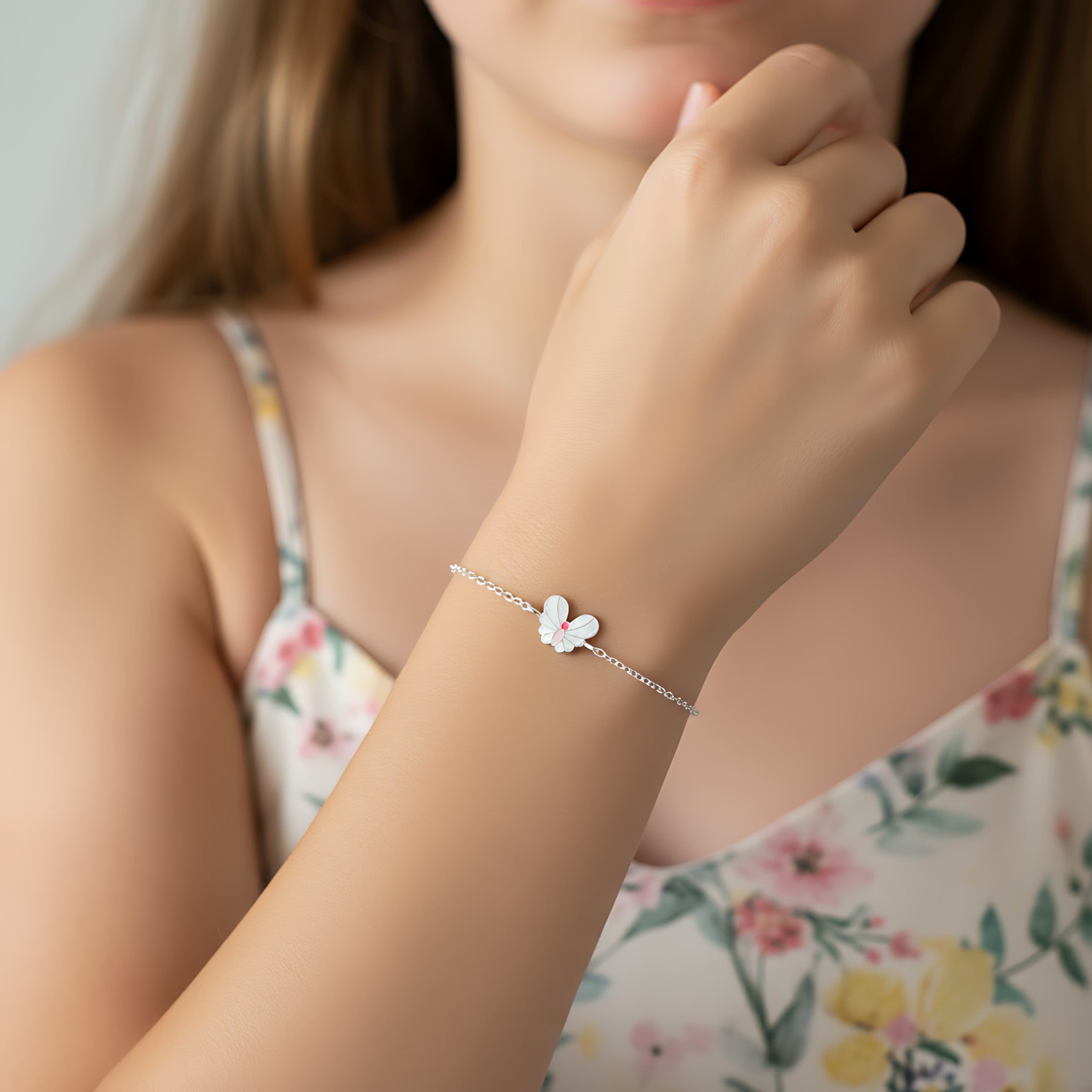 Young girl wearing a floral dress and silver butterfly bracelet against a light blue background