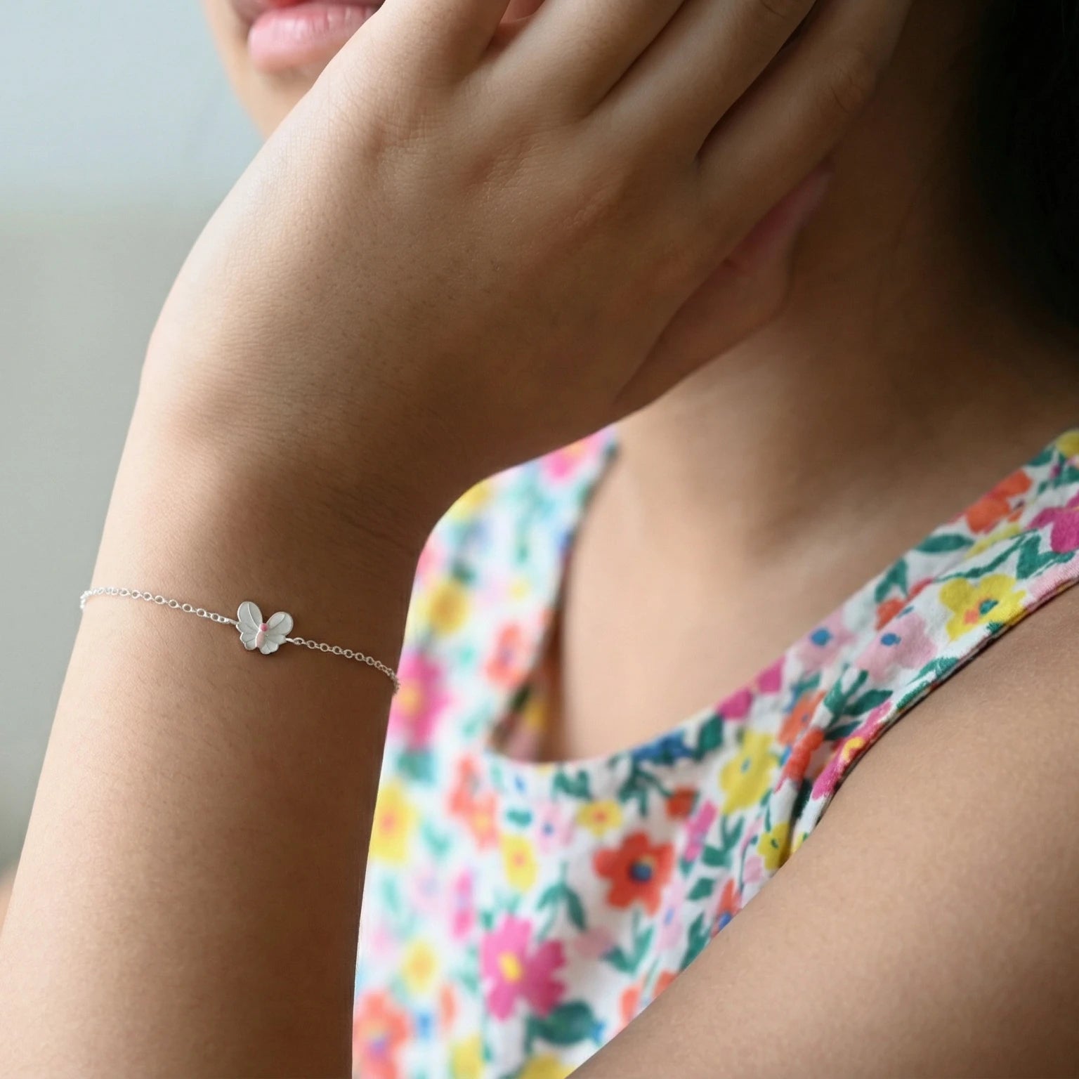 A young girl wearing a silver butterfly charm bracelet on a plain background